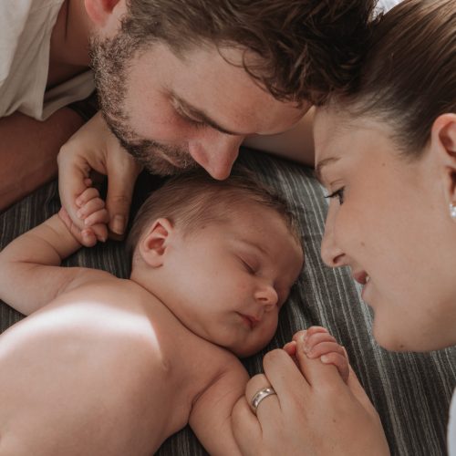 Baby mit Eltern, liegend auf dem Bett, Hände haltend